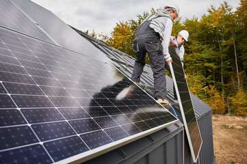 Men electricians installing solar panel system on roof of house. Workers in helmets lifting up...