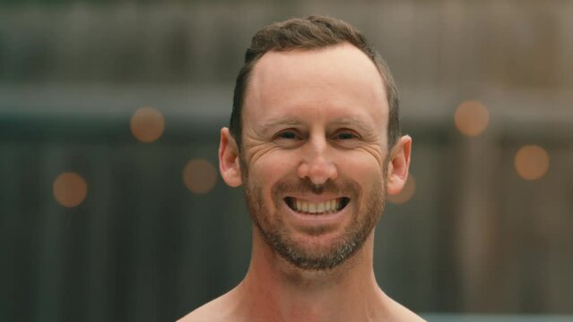 Man drenched with huge water balloon splash in extreme 4k 800fps slow motion, close up face with string light background