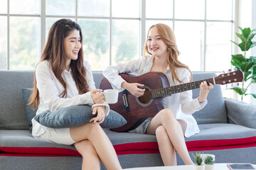Two asian couple beautiful woman playing acoustic guitar, sing folk song together sitting on sofa...