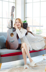 Two asian couple beautiful woman playing acoustic guitar, sing folk song together sitting on sofa...