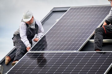 Electricians building photovoltaic solar module station on roof of house. Men technicians in...