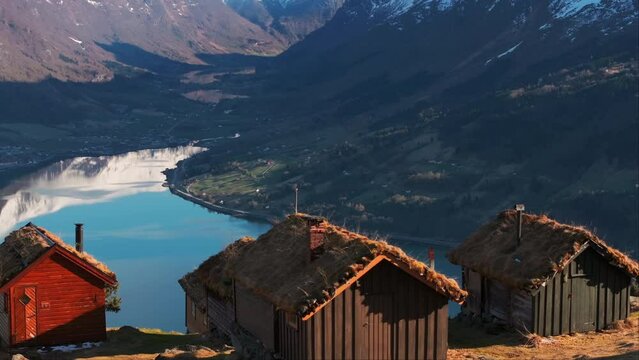 Idyllic old mountainside cabins in sunset glow overlook Loen valley; drone reveal