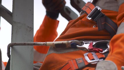 Construction worker in orange safety gear securing a harness at a high altitude site, focus on gear details
