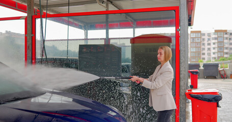 Young woman washing her car with water at a car wash