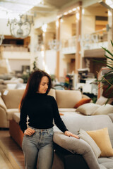 Young woman choosing sofa and pillow in furniture store