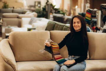 Obraz premium The woman chooses the fabric on the sofa. A young women looks at tissue samples. Selects the color of the sofa. Textile industry background. Tissue catalog.