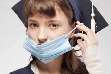 Graduation girl wearing gown and cap. Female student putting on protective face mask.