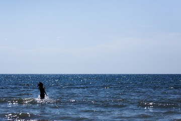 Silhouette of a person wading in the shimmering ocean under a clear blue sky