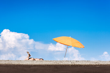 Young woman relaxing under vibrant orange beach umbrella on a sunny day