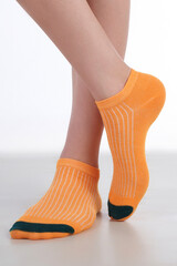 Close-up shot of a women's legs in short orange striped printed socks. A girl in ankle cotton socks stands on a white background. Front view.