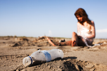 Environmental concept of pollution with a blurry woman on a beach next to a plastic bottle