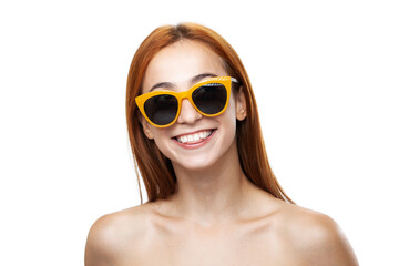 Close-up of a cheerful young redhead woman wearing stylish yellow sunglasses and showing a radiant smile against a white backdrop