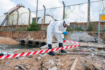 Man Scientists biologists or researchers in protective suits taking water samples from waste water from industrial. Experts analyze the water in a contaminated environment.