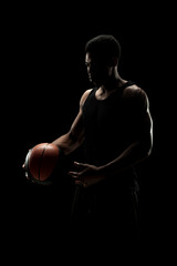 Basketball player holding a ball against black background. Serious concentrated african american...