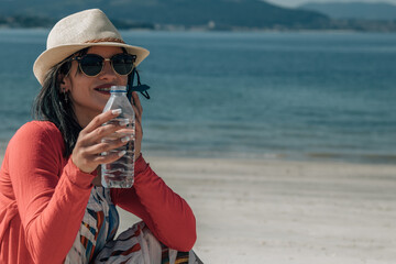 young woman with phone and bottle of water on the beach