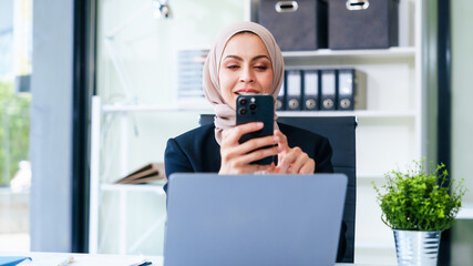 Dynamic Muslim businesswoman, adorned in a hijab, orchestrates success through her mobile device at...