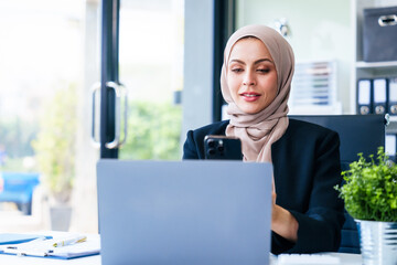 Dynamic Muslim businesswoman, adorned in a hijab, orchestrates success through her mobile device at her desk. market order, bootstrapping, USP, fiduciary responsibility, business world with finesse.