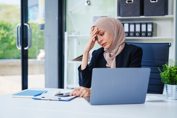 Diligent Muslim businesswoman, donning a hijab, diligently works at her desk. Amidst her...