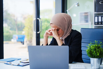 Diligent Muslim businesswoman, donning a hijab, diligently works at her desk. Amidst her...