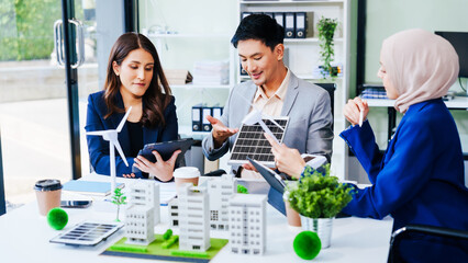 Trio of businesspeople, including a middle-aged Asian man and woman, strategize at their desk, prioritizing sustainability renewable energy adoption, waste reduction, and eco-friendly practices.
