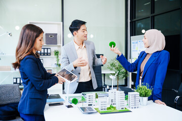 Trio of businesspeople, including a middle-aged Asian man and woman, strategize at their desk, prioritizing sustainability renewable energy adoption, waste reduction, and eco-friendly practices.