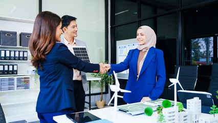 Three businesspeople convene at a desk with handshakes. middle-aged Asian man and woman discuss...