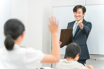 塾・学校の教室で小学生・中学生の子供に勉強を教える男性講師・教師
