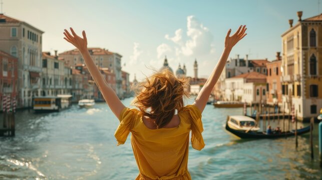 Giovane donna che si diverte a braccia aperte in libert&agrave;, vista da dietro, durante una vacanza con sullo sfondo la citt&agrave; di Venezia, Italia