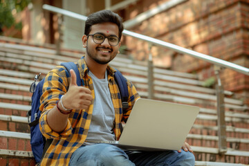 Happy Indian student with laptop giving a thumbs up on stairs
