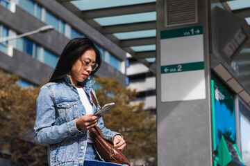 Asian tourist teenage girl at train station using smartphone map, social media check-in, or buy...
