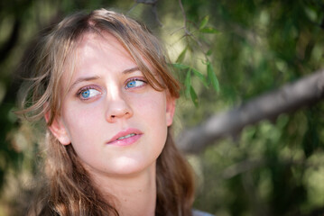 Closeup of a blonde girl posing in a park or natural area.