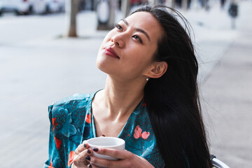 Asiatic woman drinking cup of coffee and dreaming