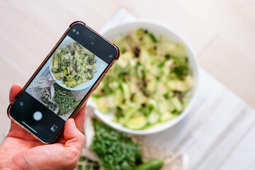 Over-the-shoulder view of a person photographing a bowl of freshly made salad with a smartphone, capturing a moment of healthy lifestyle.