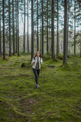 Caucasian young woman walking in a green scandinavian forest with outdoor clothes. 