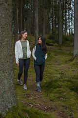 Fototapeta premium Two young women asian and european going for a walk in nature with green forest in the background