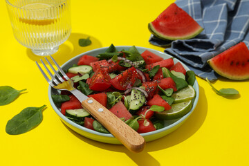 Fresh watermelon salad in a bowl with a glass of lemonade on a yellow background