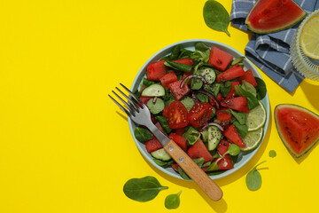 Fresh watermelon salad in a bowl with a glass of lemonade on a yellow background