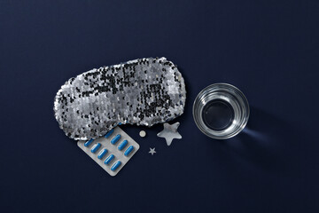 Sleep mask, pills and glass of water on blue background, top view