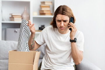 Young Man Unpacking Online Shopping Item, Looks Confused While Talking On Phone, Problem With...