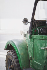 Detail of an old, worn, and dirty off-road vehicle. Rearview mirror. Green colored car. Isolated.