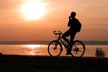 Fototapeta premium The silhouette of a cyclist at sunset on the lakeshore.