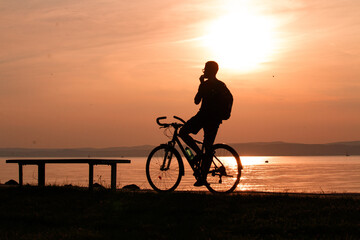 The silhouette of a cyclist at sunset on the lakeshore.