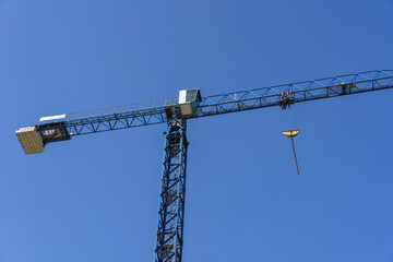 Construction crane against the sky. Tall blue tower crane. Construction site. Industrial crane equipment at a construction site. Technology for transporting materials to heights. Housing construction.