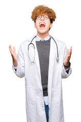 Young handsome doctor man wearing medical coat crazy and mad shouting and yelling with aggressive expression and arms raised. Frustration concept.