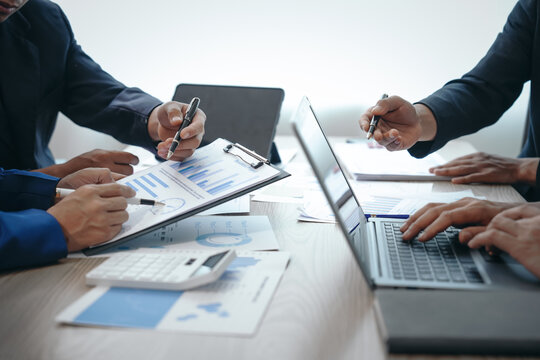 A professional business team meeting in formal suits, working at desks with financial papers, calculators, and laptops. Close-up of hands. Discussion on revenue, brand, sales, agenda, capital
