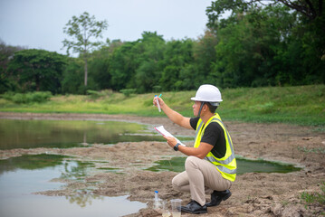 Environmental engineer Sit down next to a well and looking at the glass tube of water sample to analysing check the quality and contaminants in the water source.