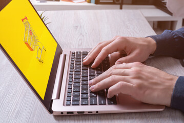 Fototapeta premium Hands typing on laptop keyboard with shopping cart on display. Concept image of online shopping. Modern digital retail experience