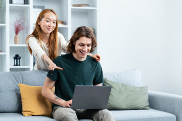 Couple Using Laptop On Sofa At Home: A young couple, woman and man, happily engaged with a laptop...