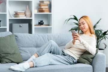 Young Woman Relaxing On Sofa With Smartphone, Casual Home Lifestyle, Comfortable Living, Modern...