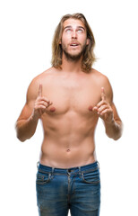 Young handsome shirtless man with long hair showing sexy body over isolated background amazed and surprised looking up and pointing with fingers and raised arms.